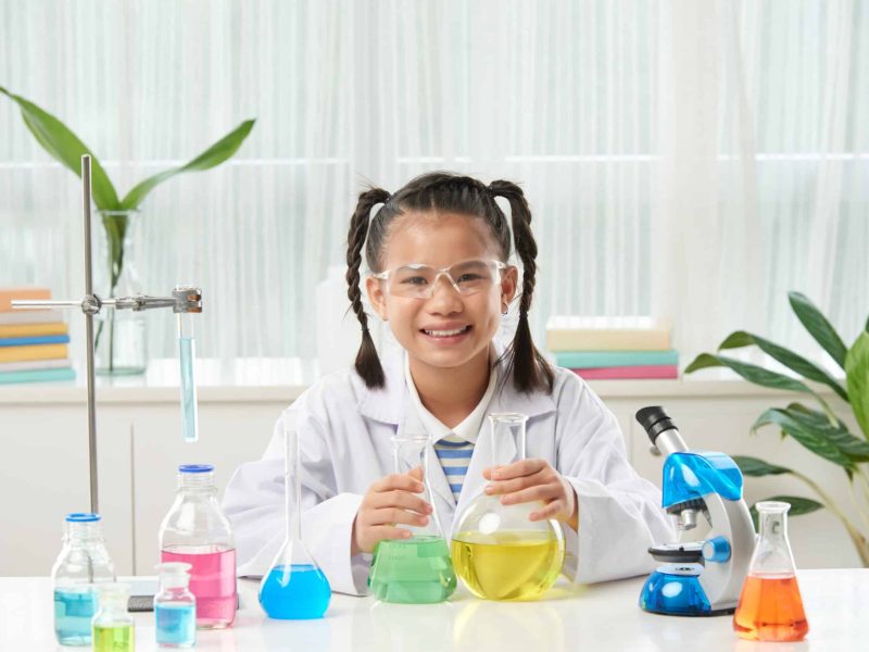 Flasks with colorful liquids on table of schoolgirl