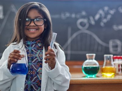 Portrait of a little girl in a lab coat doing a science experiment in a lab.