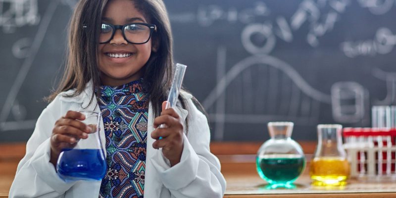 Portrait of a little girl in a lab coat doing a science experiment in a lab.